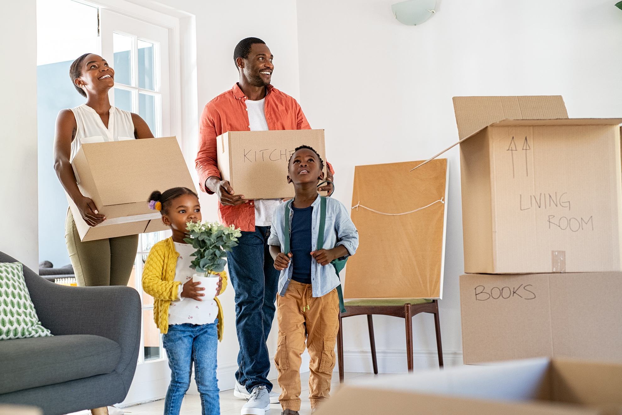 Beautiful african american family with two children carrying boxes in a new home. Cheerful mature mother and mid adult father holding boxes while entering new home with son and daughter. Happy son and daughter helping parents relocating in new house with copy space.
