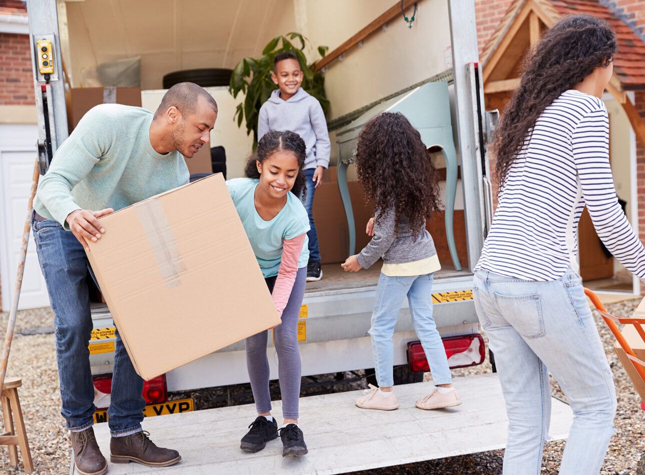 Family Unloading Furniture From Removal Truck Into New Home